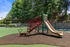 Charming playground with slide and shaded picnic area surrounded by lush greenery in a welcoming community park.