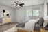 Elegant bedroom showcasing a cozy bed with plush pillows, modern artwork, and a sleek ceiling fan, enhanced by natural light from large windows with vertical blinds.
