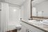 Elegant bathroom featuring a modern vanity with granite countertop, large mirror, and pristine white bathtub.