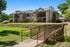 Charming apartment complex surrounded by lush greenery and featuring a serene wooden footbridge, ideal for comfortable living.