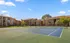 Charming apartment complex with inviting tennis court and lush green surroundings under a clear blue sky.