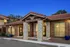 Charming apartment complex with rustic stonework and inviting entrance under a twilight sky, featuring red-tiled roofing and lush planters.
