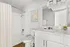 Bright and modern bathroom featuring a pristine white vanity, elegant fixtures, and a sleek glass-fronted light fixture.