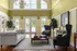 Elegant living room with high ceilings, large windows, and luxurious furnishings, offering a poolside view through French doors.