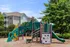Charming apartment complex with a colorful playground, ideal for families, surrounded by lush green trees.