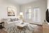 Elegant living room with a cozy cream sofa, artistic wall decor, and large windows for natural light.