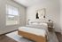 Chic and airy bedroom with modern artwork, featuring a plush bed, stylish lamps, and a large window accentuating natural light.