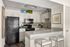 Modern kitchen with sleek black appliances, white cabinets, and a chic mosaic backsplash, featuring a stylish breakfast bar with two stools.