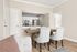 Elegant dining area with a cozy wooden table, plush white chairs, and a view into a modern kitchen with stainless steel appliances.