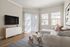 Bright and modern living room with natural light, featuring a sleek white sofa, a chic glass coffee table, and a mounted flat-screen TV.