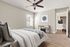 Bright and welcoming bedroom with a modern ceiling fan, elegant decor, and a view into a chic kitchen space, offering comfort and style.