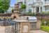 Charming outdoor patio featuring a stone fireplace, sleek barbecue grill, and comfortable seating, set against a backdrop of a stylish apartment building.