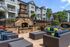 Charming outdoor seating area with a stone fireplace surrounded by lush gardens at a modern apartment complex.
