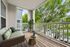 Chic and serene apartment balcony featuring cozy seating, vibrant greenery, and a refreshing view of lush trees.
