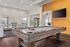 Modern recreation room with a stylish pool table, vibrant orange accent wall, and sleek bar seating overlooking a bright, inviting space.