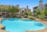 Inviting apartment complex with a sparkling outdoor pool, surrounded by lush greenery and modern architecture under a clear blue sky.