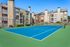 Modern apartment complex with a vibrant blue tennis court, spacious balconies, and well-maintained greenery.