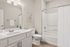 Elegant bathroom featuring sleek white cabinetry, a modern sink, and a stylish bathtub with curtain, highlighted by soft lighting and tasteful decor.