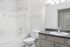 Modern bathroom featuring a sleek white bathtub, contemporary gray vanity, and large mirror with soft lighting.