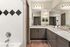 Elegant bathroom with dual sinks, large mirror, stylish black and white tiled bathtub, and inviting lighting.