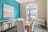 Inviting dining room with a stylish wooden table, elegant chairs, and a vibrant teal accent wall adorned with art. Natural light floods through a large, arched window, creating a cozy ambiance.