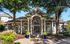 Charming residential entrance with classic columns, lush greenery, and vibrant blue planters framed by mature trees.