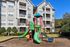 Charming apartment complex with balconies showcasing a vibrant playground set against a clear blue sky.