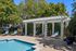 Inviting outdoor pool area featuring elegant white pergola, surrounded by lush greenery and comfortable lounge chairs.