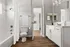 Bright and modern bathroom with elegant white cabinetry, sleek countertop, and stylish fixtures, featuring a spacious tub and warm wood flooring.