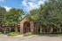 Charming red-brick building with lush landscaping and arched windows, set against a bright blue sky.