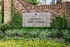 Vibrant entrance at Aston at Cinco Ranch featuring lush greenery and colorful flowers against elegant brick wall signage.