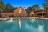 Luxurious brick clubhouse exterior with inviting pool, lounge chairs, and stylish outdoor seating area at sunset.
