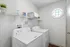 Bright laundry room with modern washer and dryer, featuring elegant shelving and a charming octagonal window.