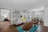 Charming open-plan living room with stylish decor, cozy bedroom view, elegant dining area by large sunlit windows, featuring modern art and colorful accents.