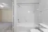 Bright and modern bathroom with a pristine white bathtub and elegant tile design, adjacent to a cozy carpeted bedroom.