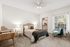 Inviting bedroom with plush carpeting, featuring a cozy bed adorned with patterned bedding, a chic wooden desk, comfortable chair, and a spacious walk-in closet.