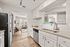 Bright and modern kitchen with sleek white cabinetry, granite countertops, and a stainless steel fridge, leading into an inviting living room with large windows and stylish furnishings.