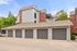 Charming apartment building featuring stylish brick and siding exterior with multiple secure garages, surrounded by lush greenery.