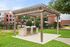Charming outdoor grilling area with stylish pergola and modern stainless steel BBQs, surrounded by vibrant greenery and inviting apartment complex backdrop.
