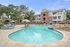 Inviting apartment complex with a sparkling pool, relaxing lounge chairs, and scenic outdoor area surrounded by brick and modern-style buildings.