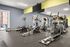 Modern apartment gym featuring state-of-the-art equipment, including elliptical machines and a rowing machine, with large mirrors and bright natural light.
