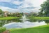 Scenic apartment complex with stunning lake view, lush greenery, and elegant architecture under a blue sky.
