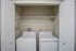 Convenient laundry nook with modern washer and dryer, enclosed by chic white doors and ample shelving above.