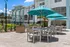 Chic apartment patio with vibrant turquoise umbrellas, modern outdoor seating, and sleek stainless steel grills, ideal for entertaining in a sunny setting.