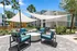 Chic outdoor patio area with modern seating and stylish shade sails, surrounded by lush greenery and palm trees, offering a relaxing retreat.