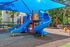 Vibrant playground with multiple blue slides and a shade cover, set in a lush, green environment.