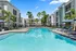 Luxurious apartment complex with a sparkling blue pool, palm trees, and cozy lounge chairs under umbrellas, perfect for relaxation and enjoyment.