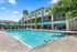 Inviting apartment complex with a sparkling pool, surrounded by lush greenery and sun loungers under vibrant umbrellas.