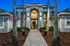 Elegant apartment entrance with modern architecture, grand arched doorway, and ambient lighting, framed by towering palm trees and vibrant potted flowers.