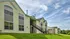 Charming apartment exterior with modern siding, large windows, and lush green landscape under a bright blue sky.